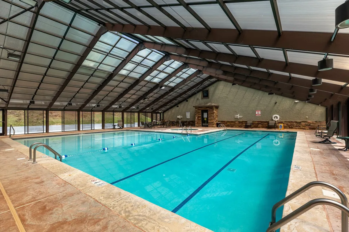 A modern indoor swimming pool with a glass roof lets in abundant natural light, while lounge chairs and a stone fireplace create a resort-like atmosphere. The pool area looks inviting for both active swims and peaceful lounging, regardless of the season.