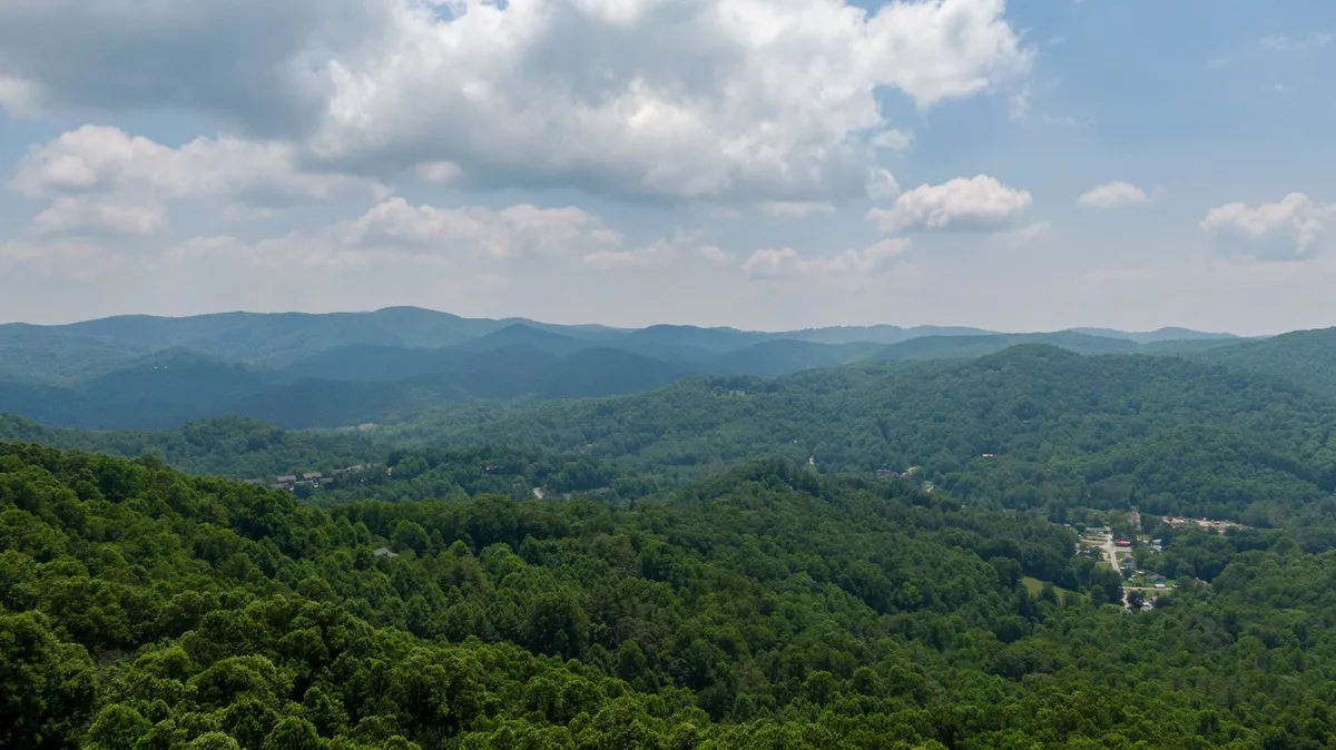 A tranquil mountain landscape stretches out under a cloudy sky, with rolling hills and dense greenery promising opportunities for hiking, photography, and quiet contemplation. The scene is serene, with a sense of openness and possibility.