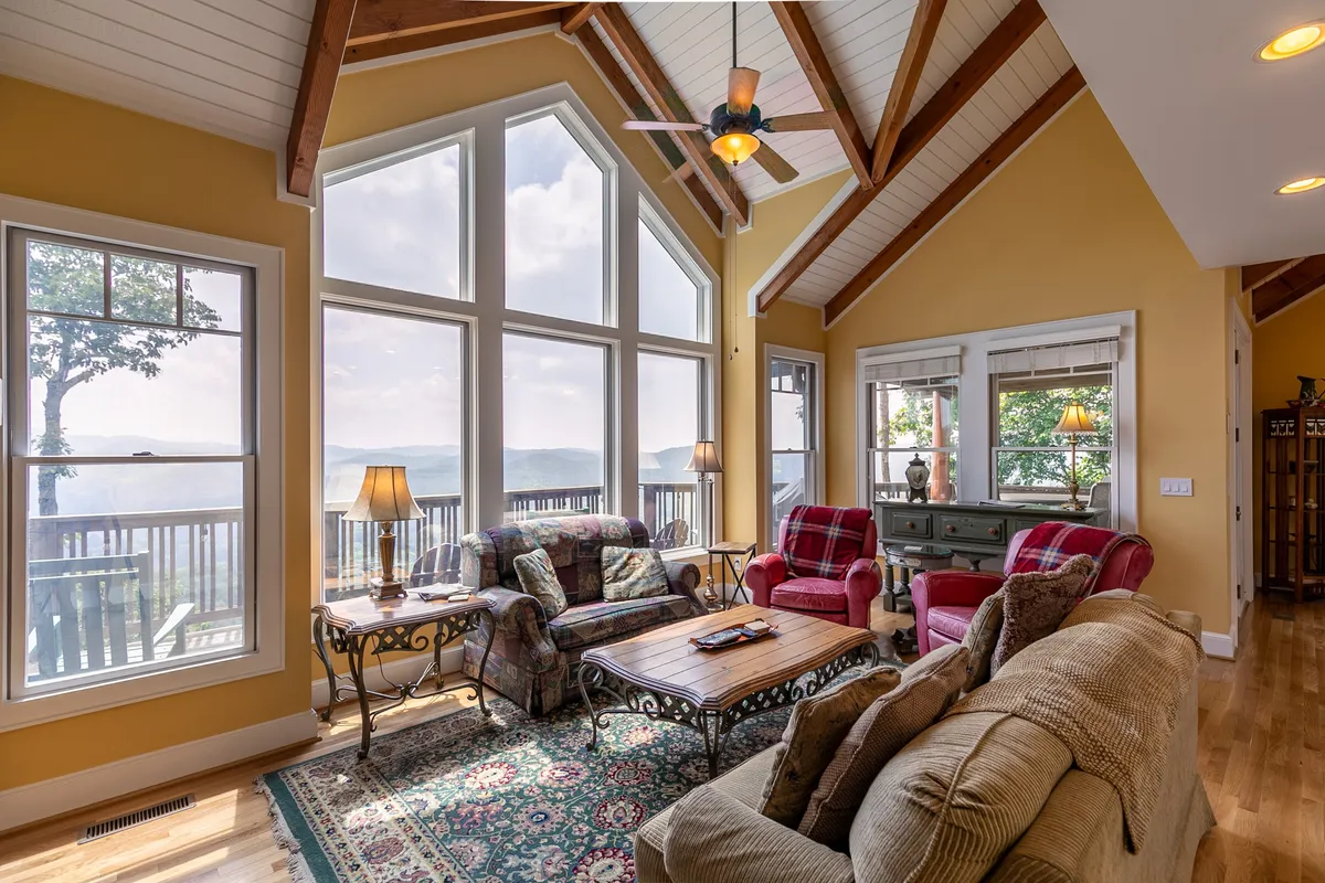 A cozy living area with large windows framing scenic mountain views. The room includes plush seating, decorative lamps, and a stylish coffee table, all arranged for comfort and socializing. The fireplace and inviting décor create a warm ambiance for winter evenings.