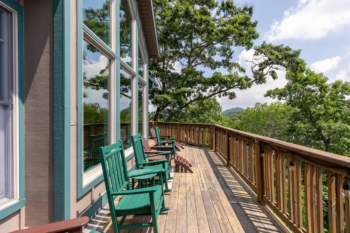 An inviting deck with green rocking chairs and a wooden railing overlooking a panoramic view of treetops and distant mountains. The scene exudes a sense of calm, ideal for relaxing and taking in the scenery during warmer months.