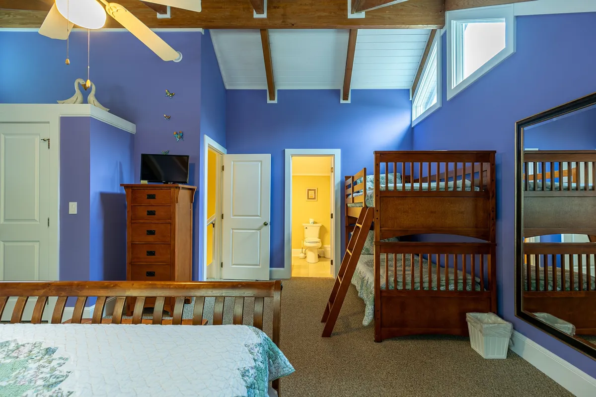 A cheerful bedroom with colorful wall decor, bunk beds, a large mirror, and a dresser with a TV. The room gives a playful vibe and is perfect for kids or groups needing additional sleeping options.