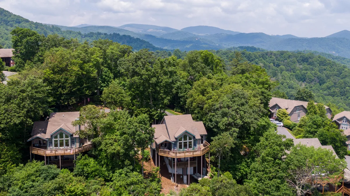 A spacious wooden deck extends from the home, bordered by large windows that look out toward a stunning panorama of mountain peaks and lush trees. The deck is surrounded by nature, making it an ideal setting for morning coffee or sunset drinks. The tranquil scenery and inviting seating area encourage relaxation and connection with the outdoors.