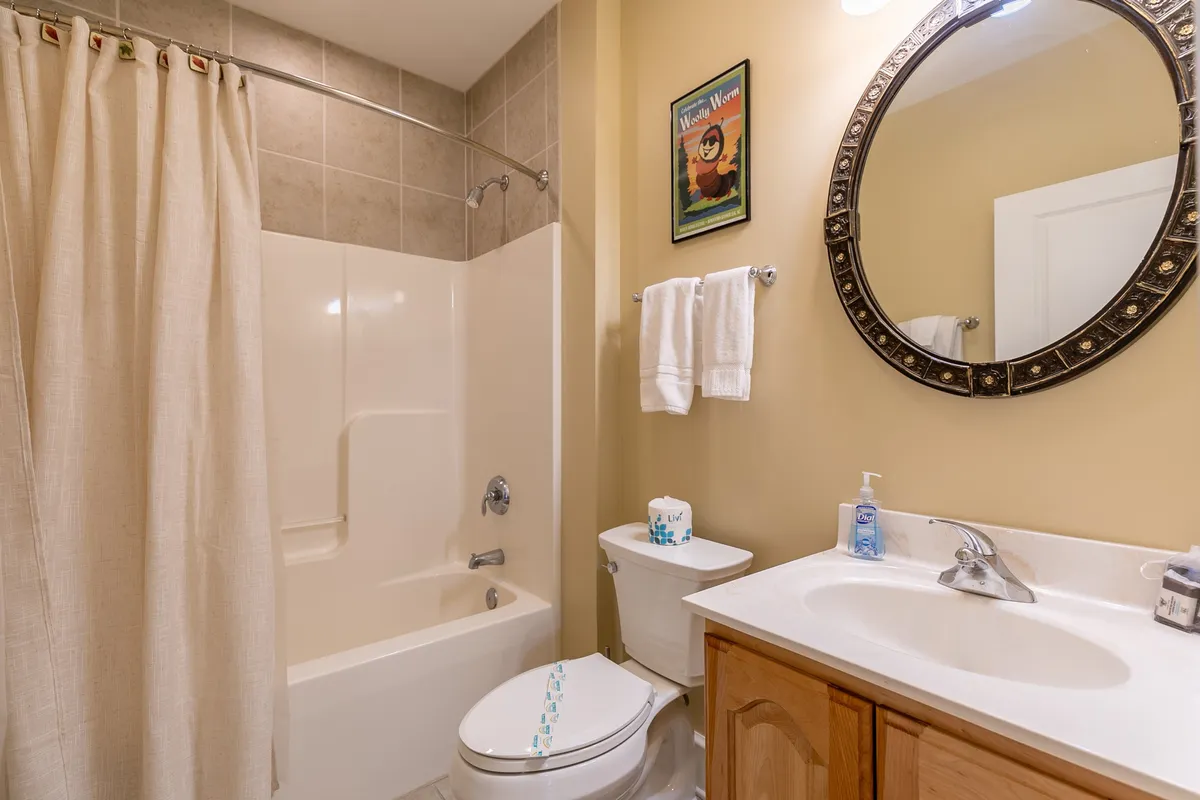 A bright and calming bathroom with a large mirror above the sink, a tub, toilet, and tasteful framed artwork. The space is well-lit and promotes relaxation and self-care routines.