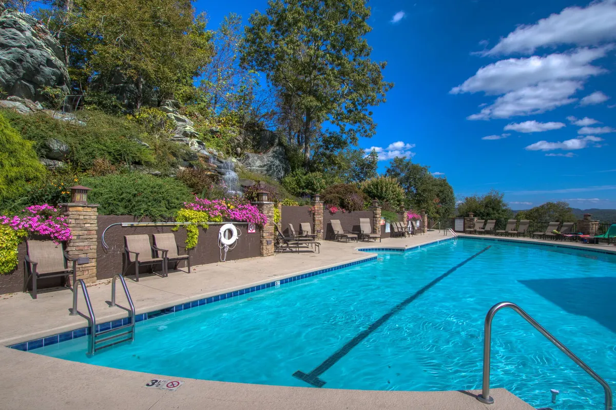 A tranquil outdoor swimming pool surrounded by lush flora, lounge chairs, and a waterfall feature. This space is perfect for summer relaxation, swimming, and socializing, all amidst a peaceful natural setting.