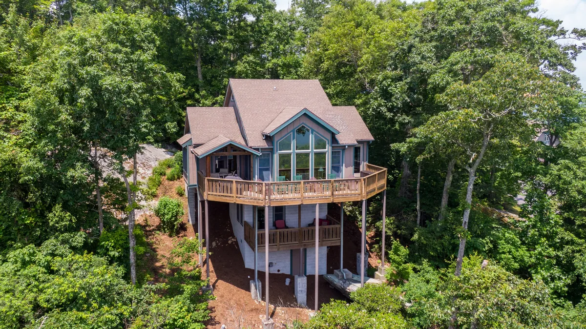 A beautiful single-family mountain home with expansive windows and a spacious wooden balcony, nestled among lush greenery in Banner Elk. The balcony offers sweeping views, perfect for relaxing, entertaining, or soaking in the serene surroundings.