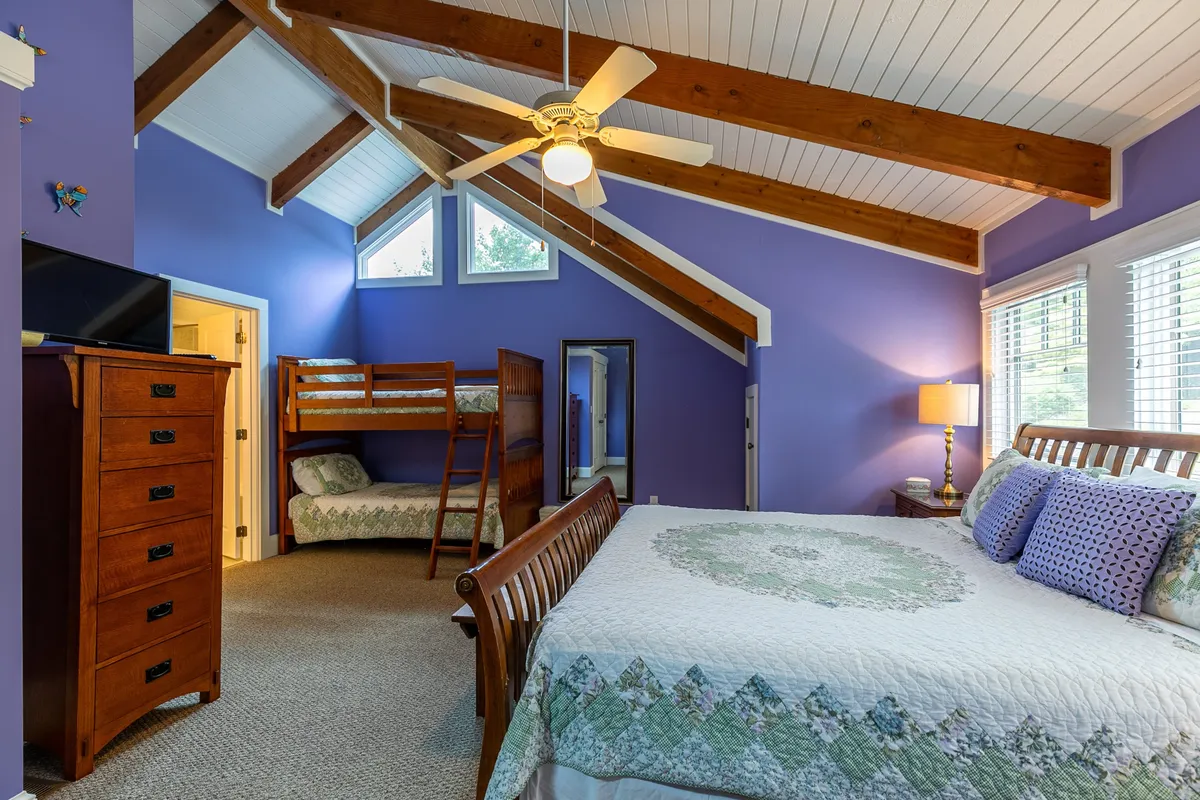 A versatile sleeping area featuring a large bed with a quilt and an adjacent set of bunk beds, complemented by a wooden dresser, ceiling fan, and warm decor. The room feels cozy and is well-suited for families or groups with children.