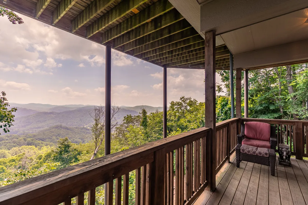 A peaceful outdoor seating area is framed by a classic wooden railing, set against a sweeping view of the mountains. The seating area invites guests to linger and take in the surrounding beauty, with seasonal foliage and a sense of serenity permeating the space.