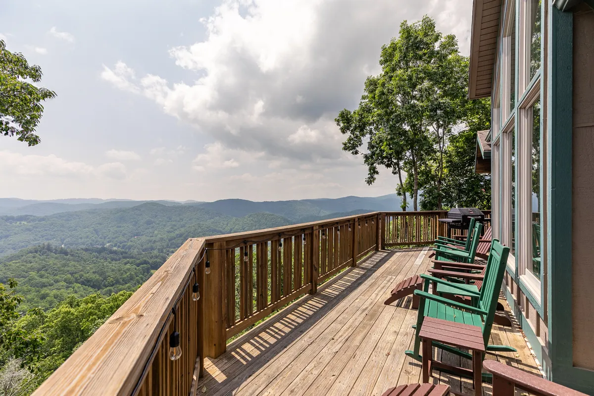 The main deck with comfortable outdoor seating, a wooden railing, and expansive views of the rolling Blue Ridge Mountains. The space is perfect for evening drinks, stargazing, or simply soaking in the tranquil mountain air.
