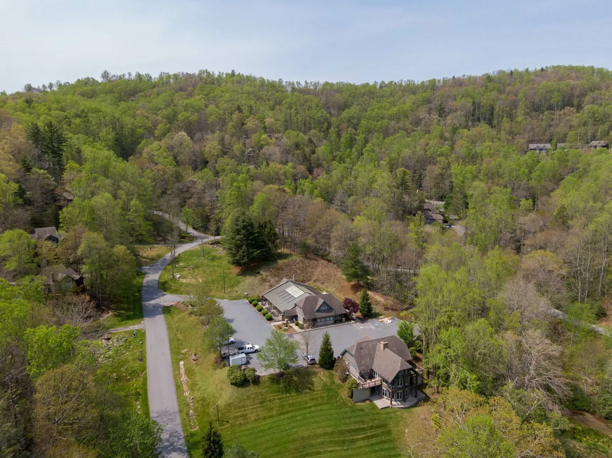 A wide-angle view of gentle green hills with a gravel road leading up to two buildings, surrounded by lush trees and open sky. The natural environment feels tranquil and far removed from urban life, perfectly embodying the retreat's peaceful and scenic setting.